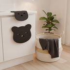 Laundry Pet Hair Remover, shaped like a smiling bear, next to a clean, hair-free dark t-shirt on a laundry basket.